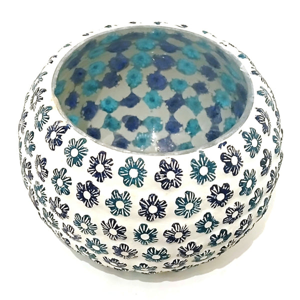 A round mosaic candle holder with a white exterior decorated with a repeating pattern of small  flowers in black and teal, and a teal and blue floral pattern on the interior.
