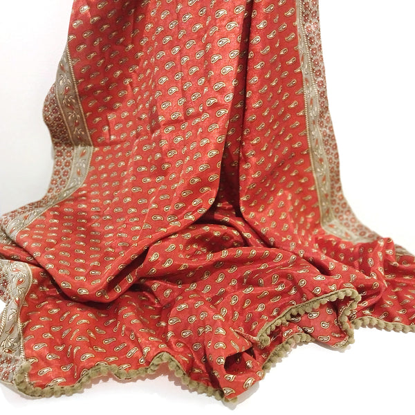 A draped terracotta red scarf featuring a small beige paisley pattern and a wide beige border with gold embroidery.