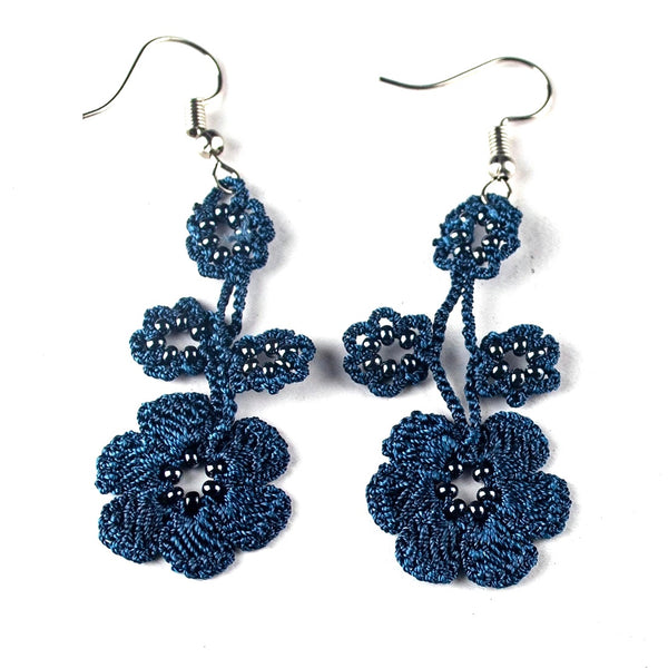 A pair of handmade dangle earrings featuring intricate blue braided floral patterns with small black beads and silver-tone fishhook ear wires.