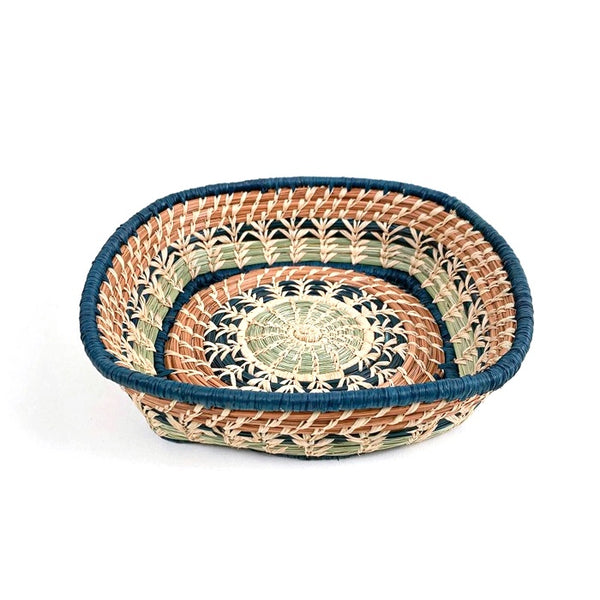 Woven basket with intricate pattern made from pine needles and colored raffia accents, available at Cerulean Arts.