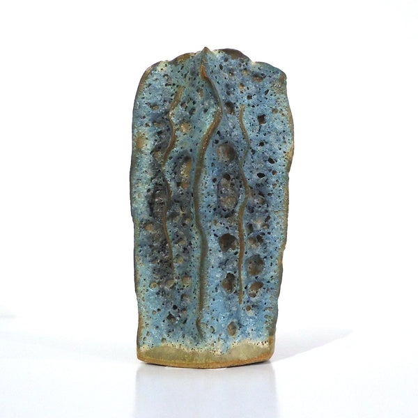 A small handmade ceramic vase with a textured surface featuring a blue-green glaze and vertical brown lines, standing upright.