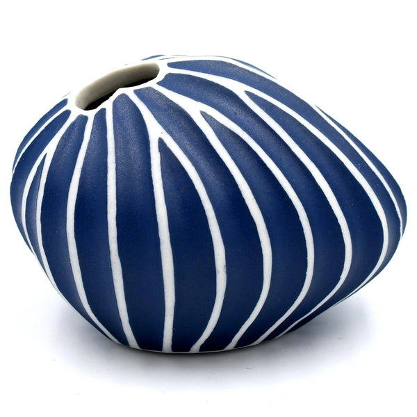 A small rounded ceramic vase with a vertical ribbed pattern in navy blue and white, featuring a small opening at the top.