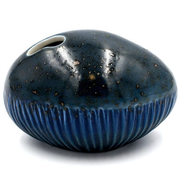 A small rounded ceramic vase with a glossy dark blue to black glaze speckled with brown, featuring a ribbed lower half and a small hole near the top.