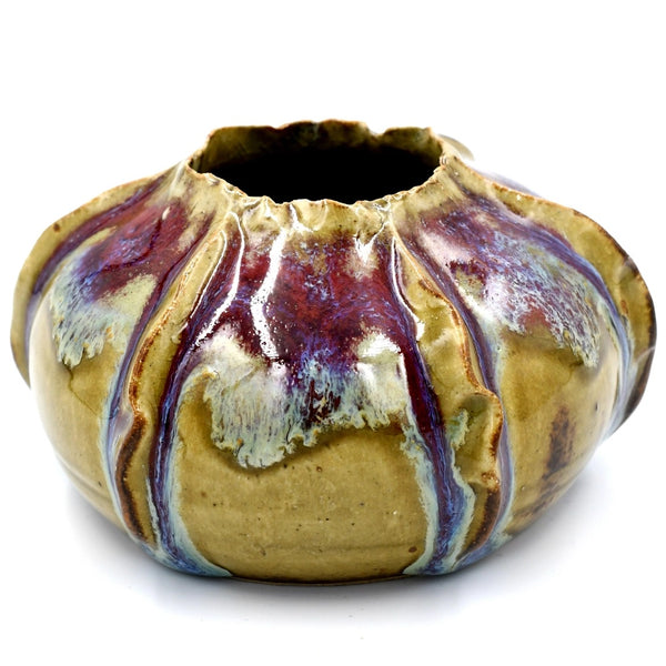 A handmade ceramic pot with a textured, ribbed exterior and a dark, open top, featuring a glossy glaze with swirls of purple, blue, and cream over a tan base.