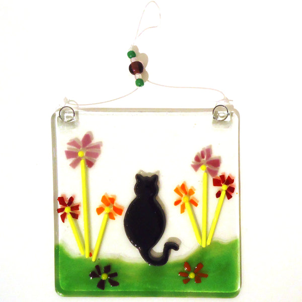 Fused glass suncatcher featuring a black cat with flowers, available at Cerulean Arts.