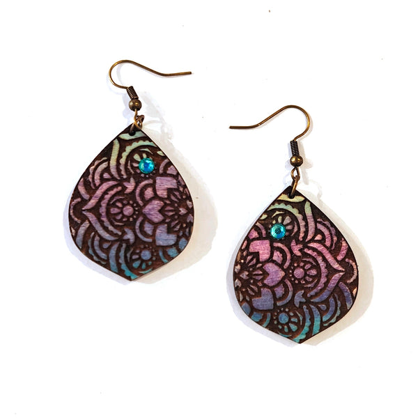 A pair of teardrop-shaped dangle earrings with intricate floral cutout patterns in purple, pink, and teal, suspended from bronze-colored fishhook wires on a white background.