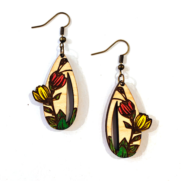 A pair of teardrop-shaped wooden dangle earrings with a hand-painted floral design of red and yellow tulips on a white wood background with dark brown wood outlines, hanging on antique bronze fishhook wires against a white background.