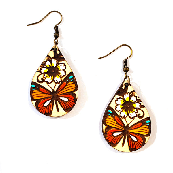 A pair of teardrop-shaped dangle earrings with a vintage stained-glass design featuring orange and red butterflies, white flowers, and turquoise accents on a cream background, suspended from bronze-colored fishhook wires.