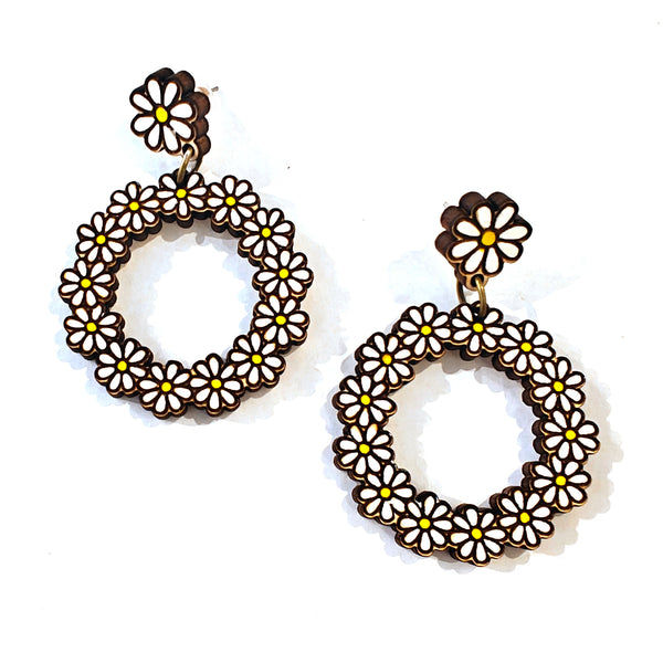 A pair of dangling hoop earrings made from small white daisy flowers with yellow centers, outlined in dark brown, shown on a plain white background.