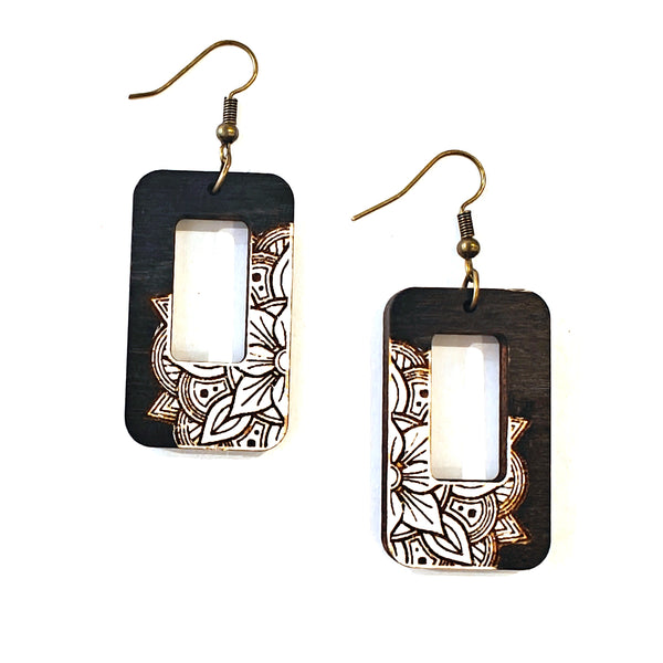 A pair of rectangular drop earrings with a dark wood-grain finish, featuring a cutout center and a white mandala pattern on the lower half, suspended from gold-tone fishhook wires on a white background.