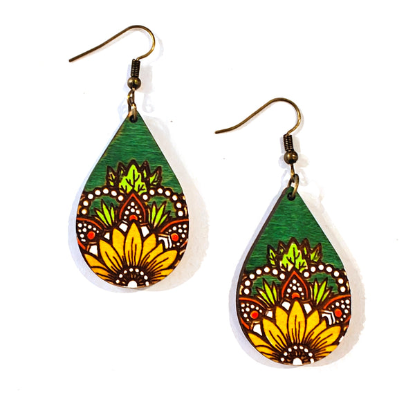 A pair of teardrop-shaped wooden dangle earrings with a hand-painted mandala design in green, yellow, orange, and white, hanging from bronze-colored fishhook wires on a white background.