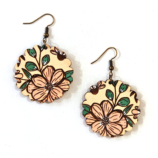 A pair of wooden dangle earrings featuring hand-painted floral designs in peach, green, and brown on a white background.