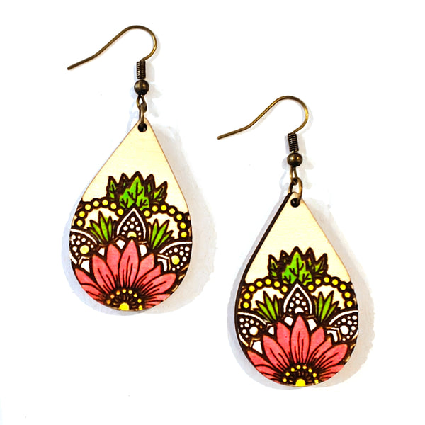 A pair of teardrop-shaped wooden dangle earrings with a hand-painted floral mandala design in pink, green, yellow, and black on a cream background, hanging from antique bronze fishhook wires.