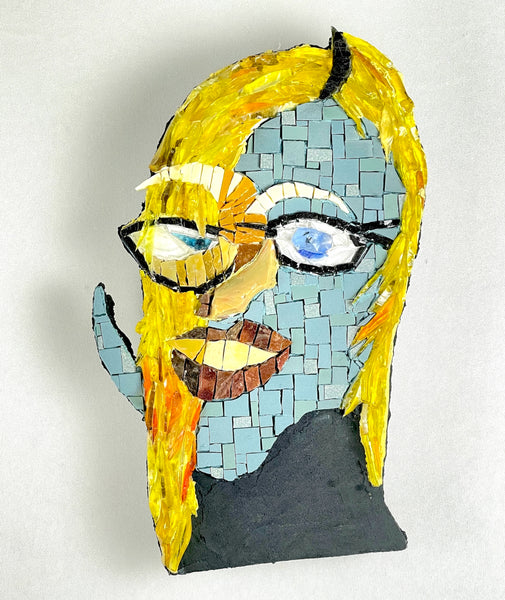 A mosaic portrait sculpture of a woman with blonde hair, glasses, a blue-tiled face, and a black top.