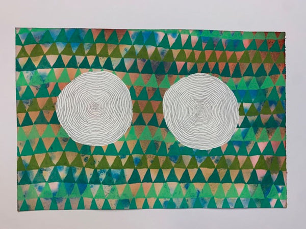 An abstract geometric art print featuring two white spiral circles on a background of green, blue, and pink triangles, displayed against a plain white wall.