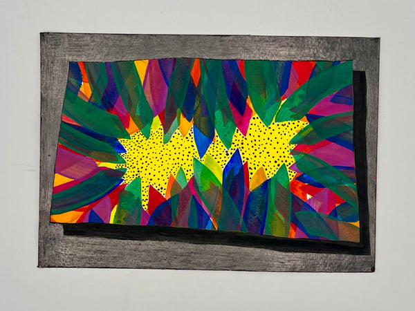 A colorful abstract artwork with two bright yellow starburst shapes, surrounded by layered green, blue, purple, red, and orange geometric patterns, mounted on a dark textured wooden frame against a light gray wall.