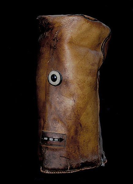 Brown leather sculpture with a central eye-like feature and mouth on a black background