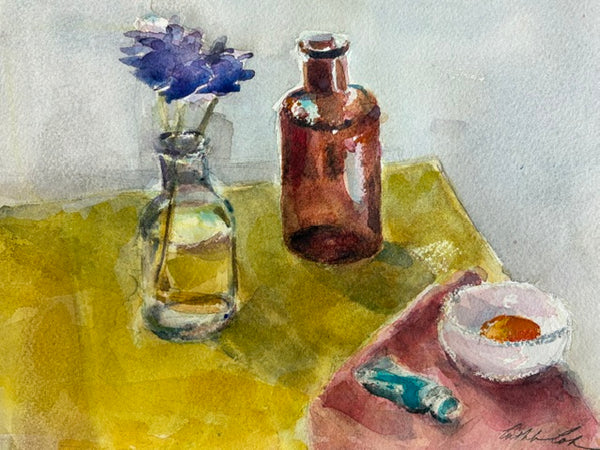 Watercolor still life painting featuring a clear glass bottle with a blue flower, an amber-brown bottle, a yellow-green tabletop, and a small white bowl with orange contents on a pink cloth.