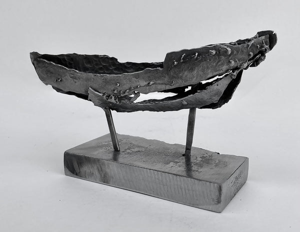 Abstract steel sculpture of a boat on two posts on a rectangular base.