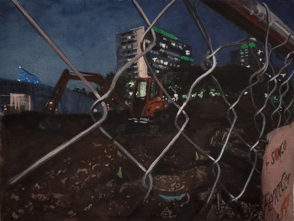 Excavator at a construction site with buildings in the background, viewed through chain-link fence.