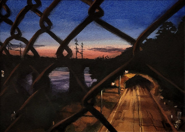 Evening scene through a chain-link fence with a bridge and sunset.