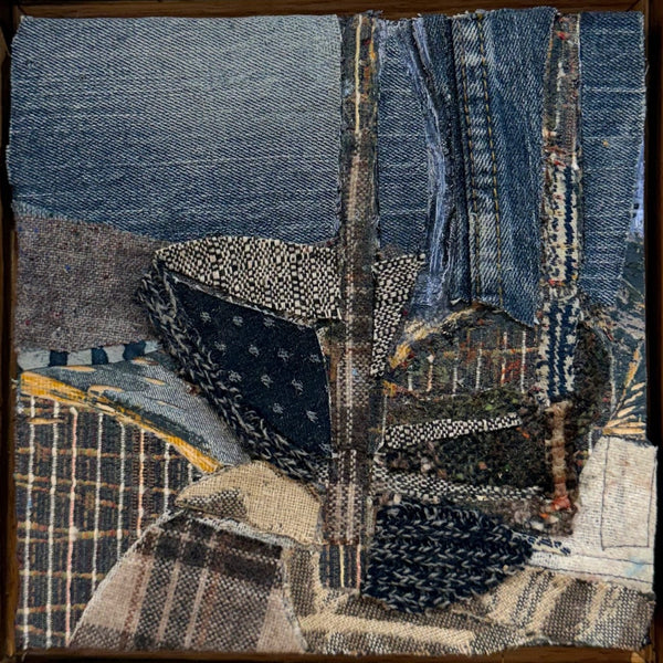 A square textile art piece featuring a collage of denim, plaid, and patterned fabric strips in blue, beige, black, and gray tones, framed by a dark wooden border.