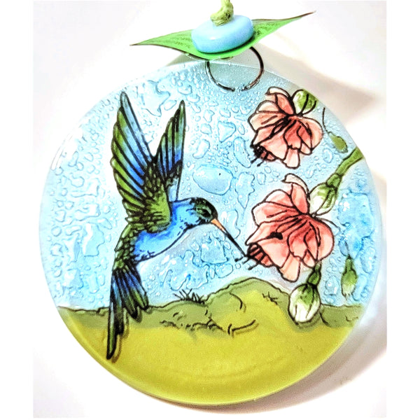 Fused glass suncatcher featuring a hummingbird hovering at pink flowers available at Cerulean Arts. 